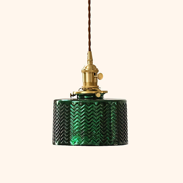 C'est une suspension en verre. La suspension est de forme cylindrique, petite avec une pièce en laiton doré et un câble tressé. La suspension est verte avec un motif zigzag. 