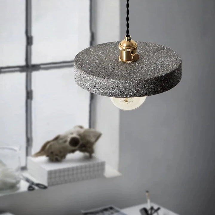 Suspension terrazzo cylindre plat industriel, lampe suspendue avec câble tressé noir et détails en métal doré. Effet terrazzo finement granulé disponible en gris clair, anthracite ou noir. Taille 16x19 cm, culot ampoule E27. Ambiance loft moderne pour toutes les pièces.