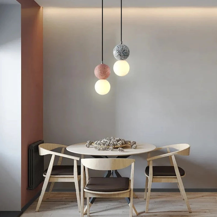 Une table avec des chaises et une table ronde avec des lumières. Une suspension en verre double globe terrazzo design scandinave, élégante et fonctionnelle pour un intérieur contemporain.