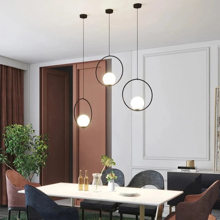 Suspension moderne avec table et chaises dans une salle à manger. Un vase de fleurs sur la table en laiton apporte une touche d'élégance contemporaine. Parfait pour éclairer et décorer votre intérieur. Ampoule LED incluse. Taille boule lumineuse : 15 cm, taille anneau : 30 cm. Convient aux salons, cuisines, chambres et salles de bains. Disponible en doré, noir ou argenté.