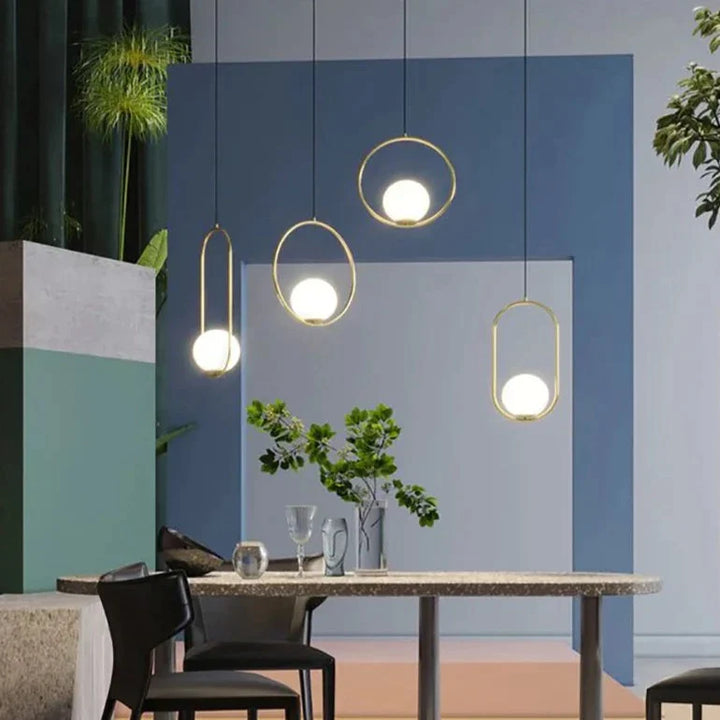 Suspension moderne boule lumineuse ovale en laiton avec table à manger et chaises, éclairée par des lampes suspendues au plafond.