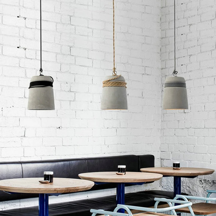 Une table et des chaises dans une pièce, avec une suspension cloche ciment et corde design scandinave suspendue au-dessus de la table.