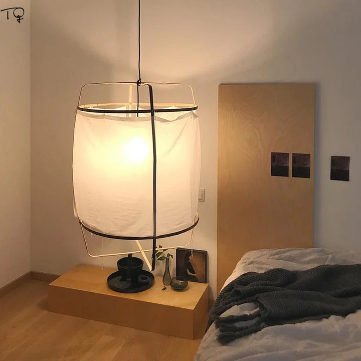 Suspension tissu lin blanc cylindre minimaliste scandinave éclairant une chambre avec une lampe sur une table près du lit, une couverture et une plante.