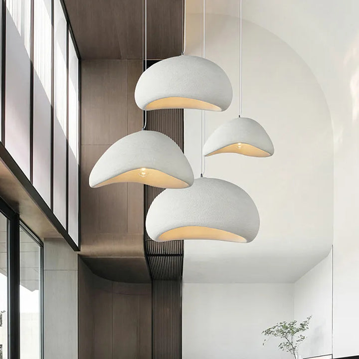 Suspension terre cuite cloche asymétrique scandinave minimaliste éclairant une pièce blanche avec des lampes suspendues blanches au plafond.