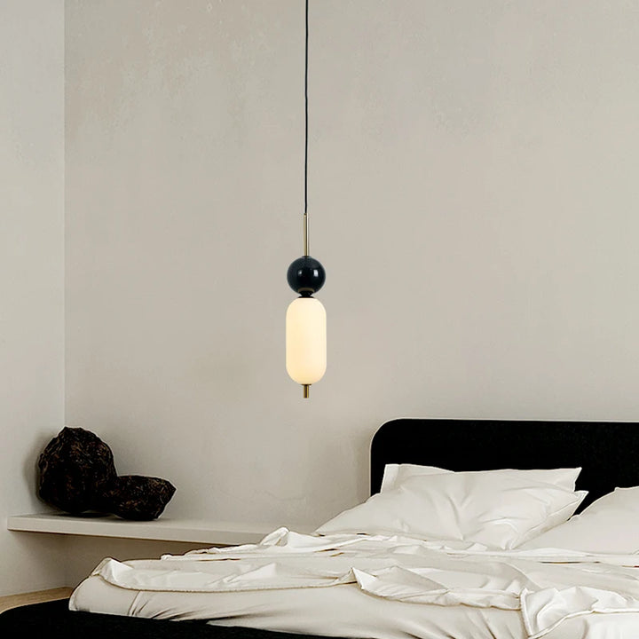 Suspension moderne bicolore boule noire marbre, lampe suspendue élégante pour intérieurs chics. Lit blanc, oreiller, mur blanc.