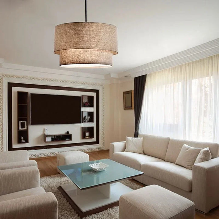Suspension en lin double cylindrique design moderne dans un salon avec un canapé et une télévision. Idéal pour éclairer votre salon avec raffinement. Disponible en nuances taupe, blanc ou noir.