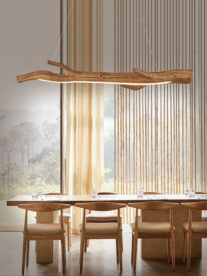 Une salle à manger avec une table et des chaises, une suspension bois branche design bohème suspendue au-dessus de la table.
