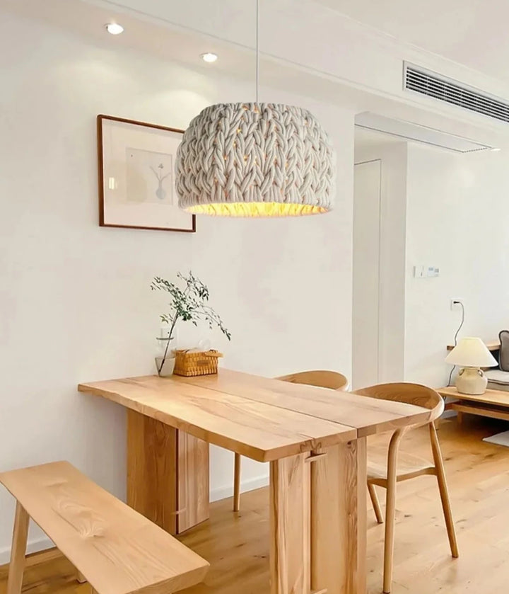 Une table avec des chaises et une lampe, une suspension cloche en corde tressée design scandinave suspendue au-dessus.