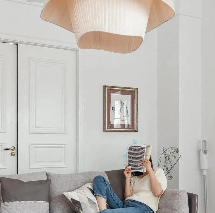 Une femme assise sur un canapé en train de lire un livre, avec une suspension tissu double vague design moderne en arrière-plan.