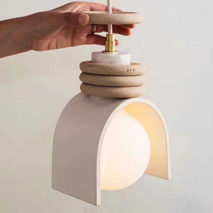 Une suspension scandinave en terre cuite avec des anneaux, tenue par une main, illustrant le design intérieur et la qualité des luminaires de LampeSuspension.com.