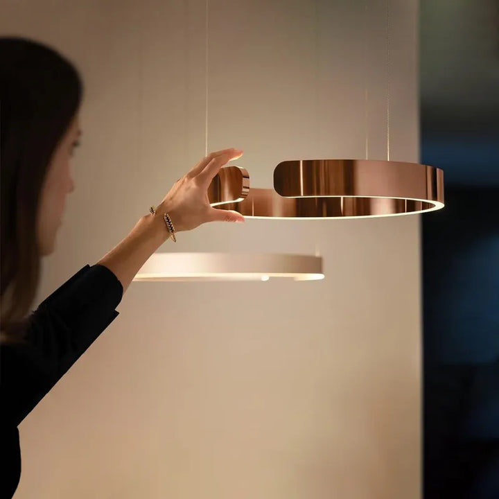 Une femme tenant une suspension métal anneau ouvert design moderne pour éclairer votre intérieur avec élégance. Disponible en différentes finitions luxueuses, cette suspension circulaire diffuse une lumière LED polyvalente, idéale pour les pièces à vivre. Sa forme minimaliste s'adapte à tous les styles, du scandinave à l'industriel. Ampoule LED incluse. Dimensions : 40 cm, 60 cm. LampeSuspension.com, Site de vente de lampes suspension pour toutes les pièces de la maison.