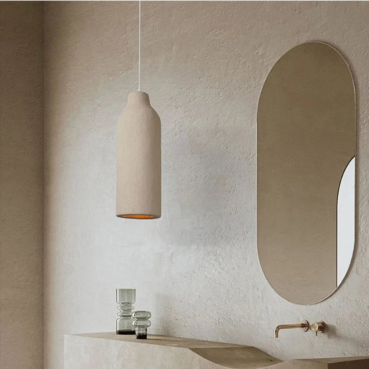Suspension allongée effet terre cuite beige bohème éclairant une salle de bain avec un lavabo et un miroir.