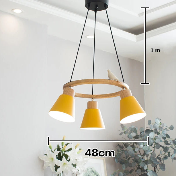 Suspension bois coloré cercle oiseau 3 lampes - un lustre jaune avec un oiseau, éclairant une pièce avec des plantes. Parfait pour une décoration scandinave contemporaine.