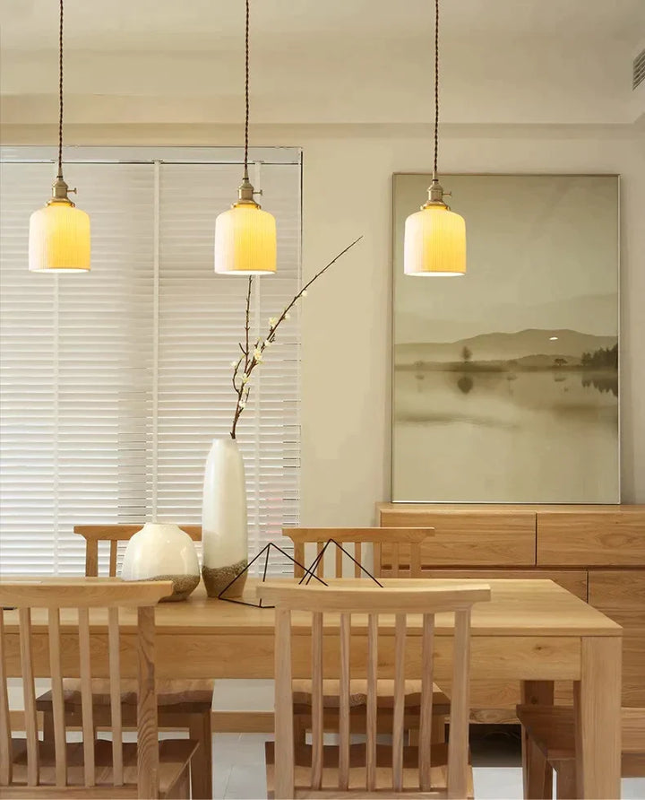 Suspension céramique blanche rainurée et cuivre cloche vintage éclairant une salle à manger avec une table et des chaises.