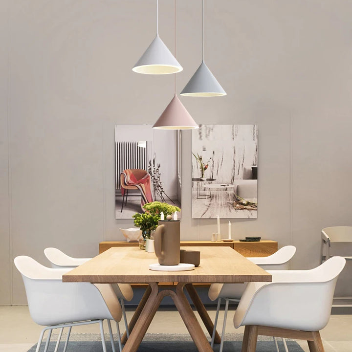 Une table avec des chaises et une lampe suspendue au plafond, dans un style nordique scandinave. Parfait pour apporter une touche de décoration tendance à votre intérieur. Disponible en différentes teintes subtiles, cette suspension métallique cône colorée s'adapte à diverses ambiances. Idéale pour éclairer votre salon, cuisine ou couloir. Ampoule LED incluse. Dimensions : 23 cm, 32 cm.