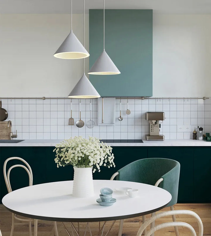 Suspension métal cône coloré design scandinave sur une table avec chaises vertes dans une cuisine