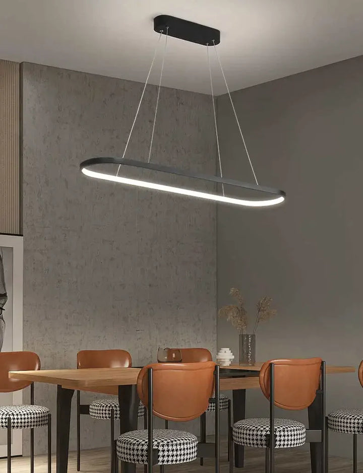 Suspension métal anneau ovale design moderne avec table et chaises dans une salle à manger. Éclairage LED intégré pour une ambiance chaleureuse ou froide. Idéal pour salon ou cuisine. Tailles disponibles: 60x20 cm, 80x20 cm, 100x20 cm, 120x20 cm.