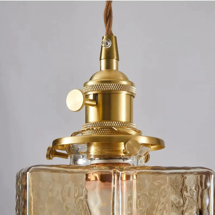 Suspension verre et métal 3 lampes art déco - Une bouteille en verre doré avec une lampe à l'intérieur.