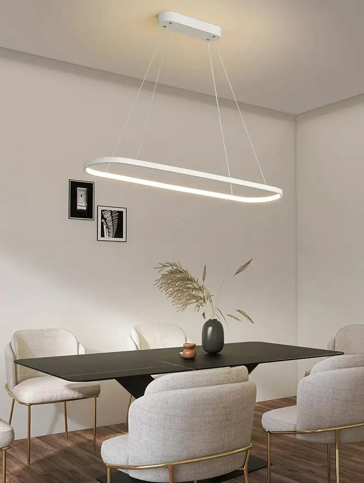 Suspension métal anneau ovale design moderne avec table et chaises noires dans une pièce.